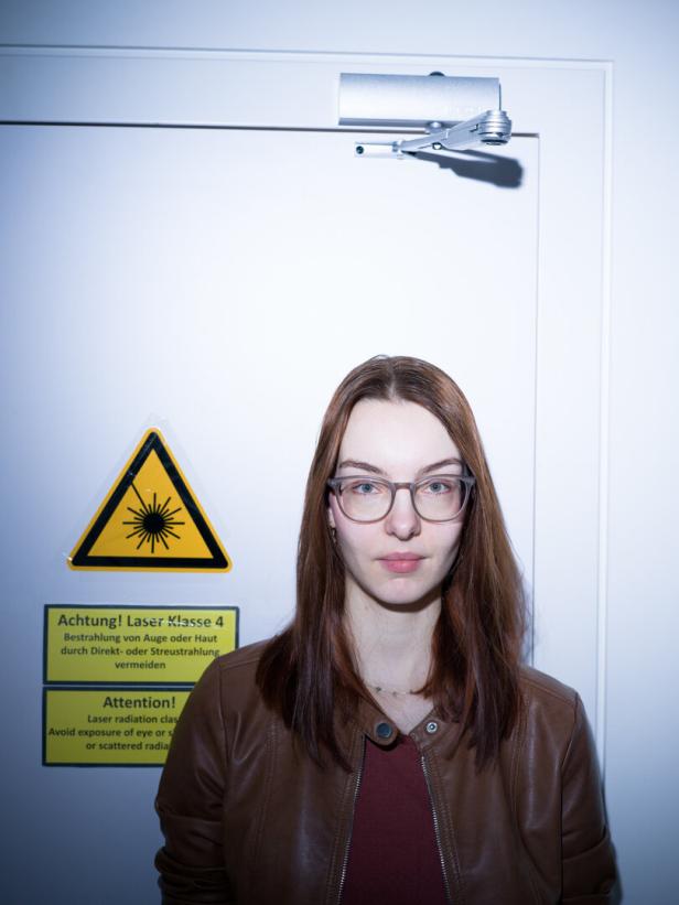 Andrea Stöllner steht vor einer Tür, auf der eine Warnung vor Laserlicht gedruckt ist