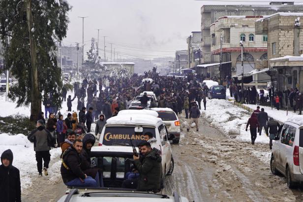 Ein Konvoi an Pickups mit Kämpfern darauf fährt durch eine schneebedeckte Stadt (Kobane).