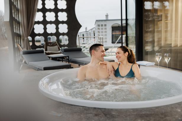 Paar entspannt in einem Whirlpool vor großen Fenstern mit Blick auf eine Stadtlandschaft