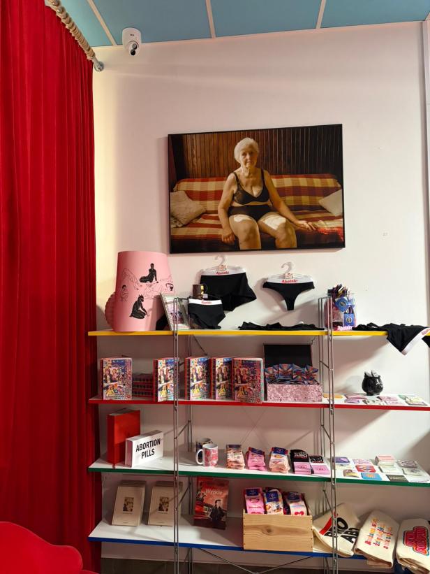Regal mit Abotak-Merchandise, Abtreibungspillen und Plakat einer älteren Frau an der Wand.