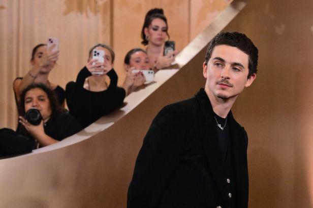 Timothée Chalamet blickt ernst drein, umringt von Menschen bei einem öffentlichen Event