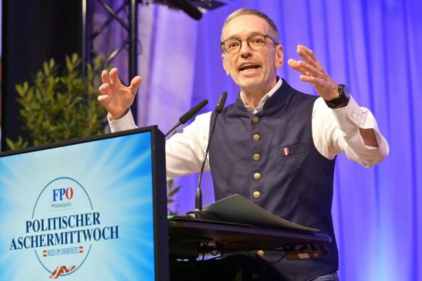 Ein Mann, es ist Herbert Kickl, mit Brille gestikuliert am Rednerpult vor einem Bildschirm mit FPÖ-Logo.