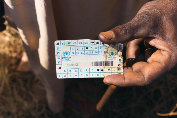 Ein Geflüchteter hält eine Plastikkarte für Lebensmittel in der Hand 