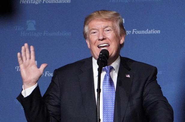 Donald Trump steht auf einer Bühne und hebt die rechte Hand