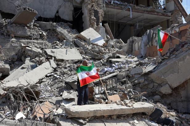 Ein Mann hält inmitten eines zerstörten Hauses eine iranische Flagge hoch