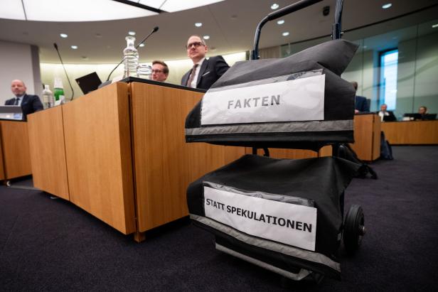 Ein Rollwagen mit den Aufschriften „FAKTEN“ und „STATT SPEKULATIONEN“ steht in einem Konferenzraum mit mehreren Personen.