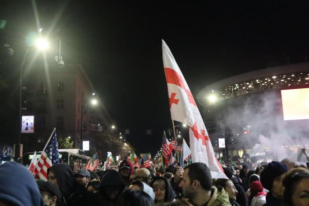 Menschenmenge, jemand hält eine Georgien-Flagge hoch, rechts Rauch