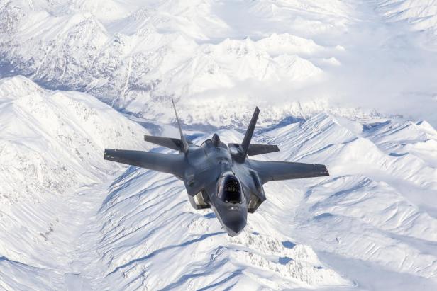 Kampfflugzeug fliegt über schneebedeckte Berglandschaft