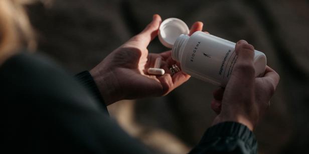 Eine Person hält eine Dose Biogena Magnesiumcitrat und entnimmt Kapseln daraus.