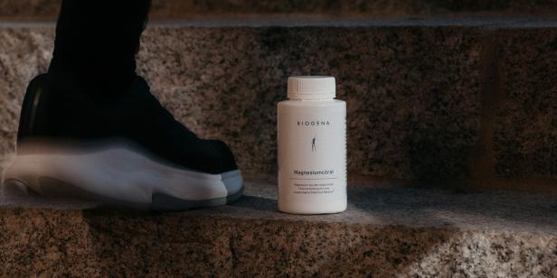 Eine Dose Biogena Magnesiumcitrat steht auf einer Steintreppe neben einem Sportschuh.