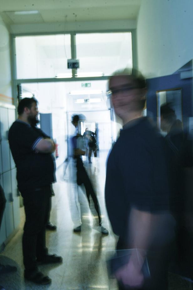 Ein Flur mit mehreren Personen, einige stehen, andere gehen, im Hintergrund ein Ausgangsschild.