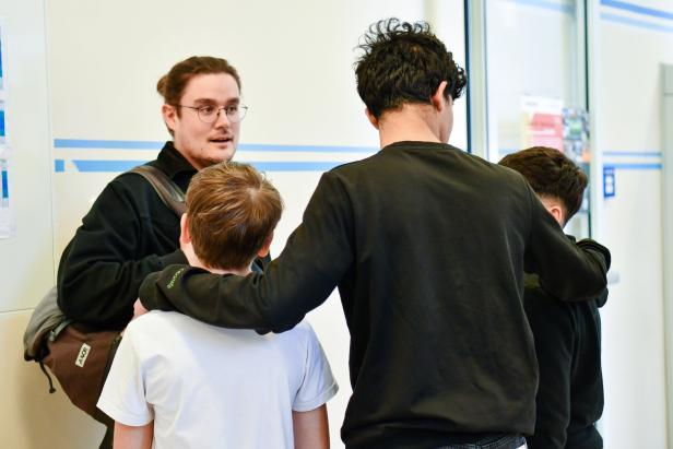 Ein Mann mit Brille spricht mit drei Jungen, von denen einer umarmt wird.