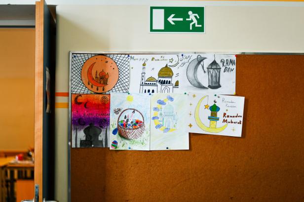 Mehrere bunte Kinderzeichnungen mit Ramadan-Motiven hängen an einer Pinnwand unter einem Notausgangsschild.