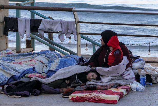 Ein Kind schläft auf einer Strandpromenade, daneben eine Frau mit einem Baby
