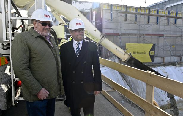 Zwei Männer stehen vor einer Baustelle und tragen einen Helm mit ORF-Logo