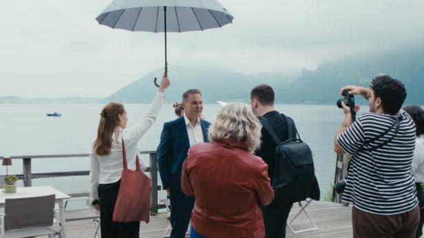 Eine Mitarbeiterin hält an einem See den Regenschirm über SPÖ-Chef Andreas Babler 