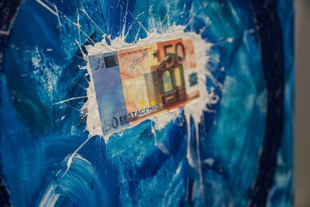 Ein 50-Euro-Schein ist mit weißer Farbe auf einer abstrakten, blau gemalten Fläche befestigt.