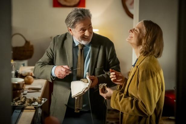 Daniel Auteuil und Jodie Foster lachen miteinander in einer Innenraum-Szene in "Paris Murder Mystery"