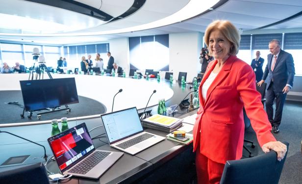 Eine Frau im roten Blazer, ORF-Chefin Ingrid Thurnher, steht lächelnd an einem Konferenztisch mit Laptops und Mikrofonen.