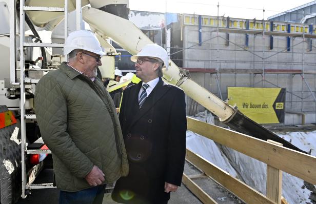 Zwei Männer mit Schutzhelmen, Pius Strobl und Alexander Wrabetz, unterhalten sich vor einer Baustelle mit Betonmischer.