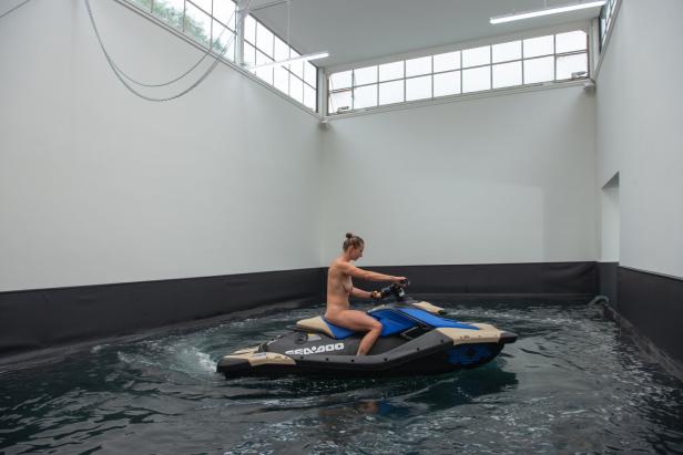 Eine nackte junge Frau fährt mit dem Jetski durch einen Innenraum-Pool