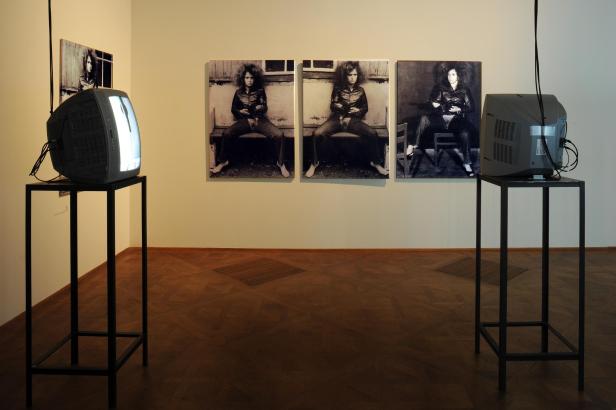 Drei Fotos der jungen Künstlerin VALIE EXPORT an der Wand eines Museums, daneben kleine TV-Monitore