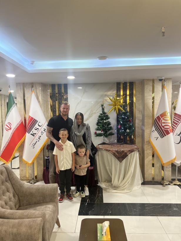 Familie Knett steht in einem Marmorgetäfelten Raum mir iranischen Flaggen Weihnachts-Dekoration