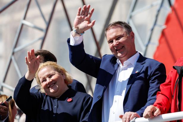 Zwei Personen in dunkler Kleidung lächeln und winken freundlich in die Menge, es sind Vizekanzler Babler und Sozialministerin Schumann beim Mai-Aufmarsch der SPÖ