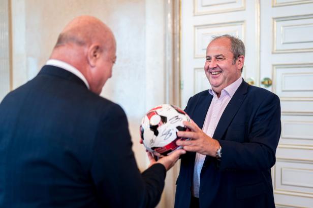 Zwei Männer im Anzug, Kanzler Stocker und ÖFB-Präsident Pröll,  überreichen sich einen signierten Fußball und lächeln dabei.