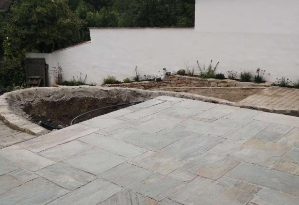 Eine neu verlegte Terrasse mit angrenzender Baugrube und bepflanztem Gartenbereich, wie sie über die Plattform Daibau vermittelt werden kann.