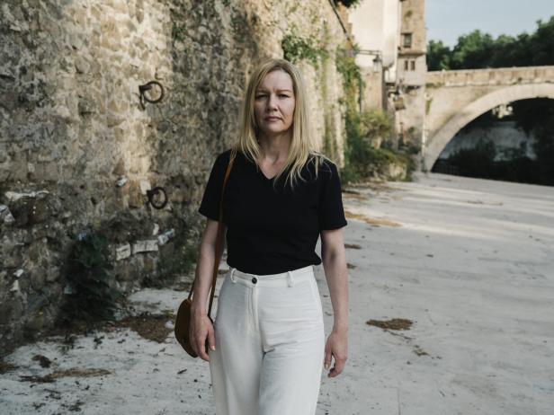 Sandra Hüller spaziert mit blonder Perücke an alten Gemäuern vorbei.