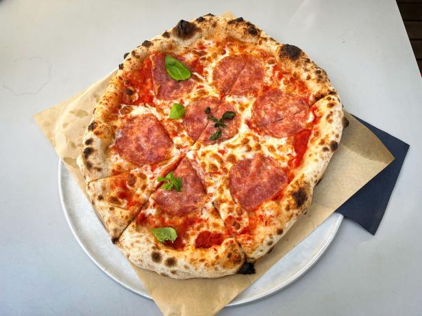 Das Bild zeigt eine mit Salami, Mozzarella und Basilikum belegte Pizza