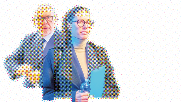 Frau mit Brille, Rollkragenpulli und Sakko, dahinter ein älterer Mann mit Brille und Anzug