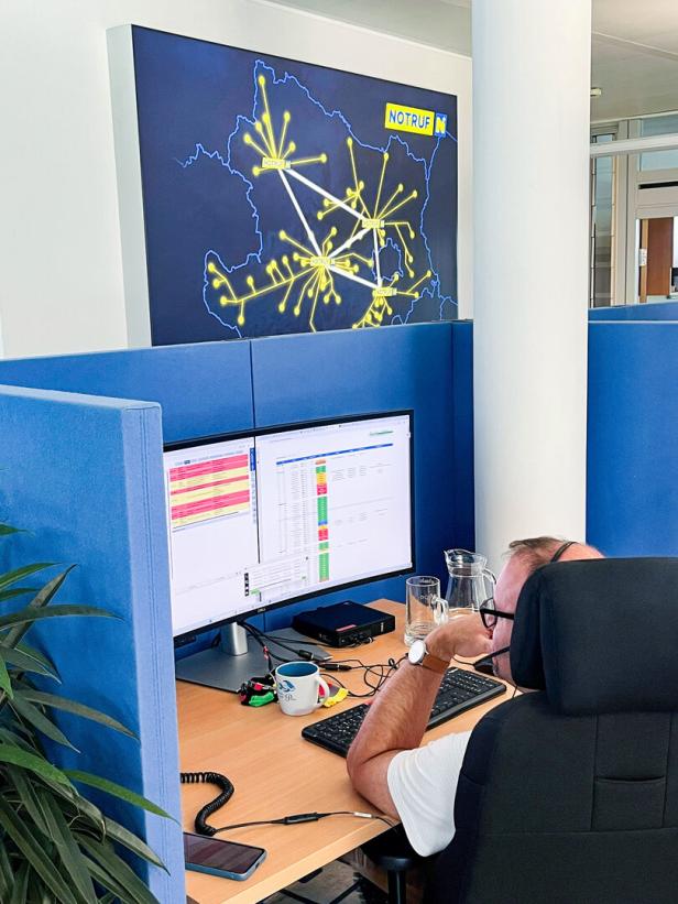 Mitarbeiter arbeitet an einem Computer im Büro, darüber eine Notruf-Karte an der Wand.