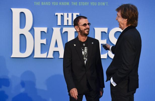 Ringo Starr (li.) und Paul McCartney vor einem blauen Plakat mit der Aufschrift "The Beatles"