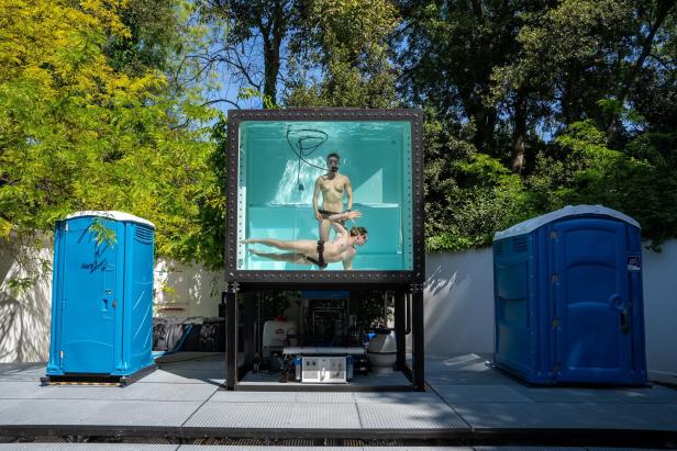 Wassertank mit tauchendem Paar zwischen zwei Mobilklos, im Hintergrund Bäume