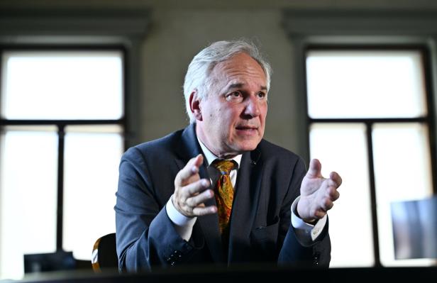 Ein älterer Mann mit grauem Haar, Nationalratspräsident Rosenkranz, trägt einen dunklen Anzug mit gemusterter Krawatte und gestikuliert während eines Gesprächs vor zwei Fenstern.