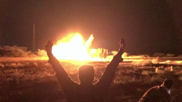 Ein Mann streckt die Arme im Jubel, dahinter eine Explosion