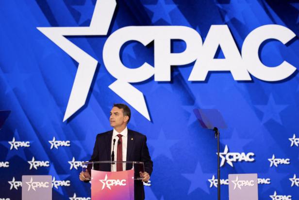 Flávio Bolsonaro steht auf einer Bühne, dahinter die Schrift "CPAC".