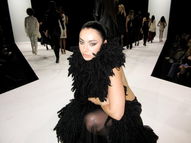 Die britische Sängerin Charli xcx, schwarz gekleidet, auf einem Mode-Laufsteg, im Hintergrund Models