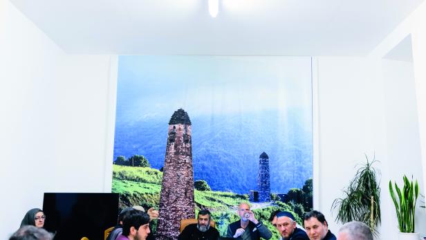 WEHRHAFT: Diskussion mit dem Rat der Tschetschenen über das schlechte Image der Community (der Autor 
in der Mitte mit Wasserglas). Im Hintergrund ein Bild eines historischen Wehrturms, der vor Eindringlingen warnte. 