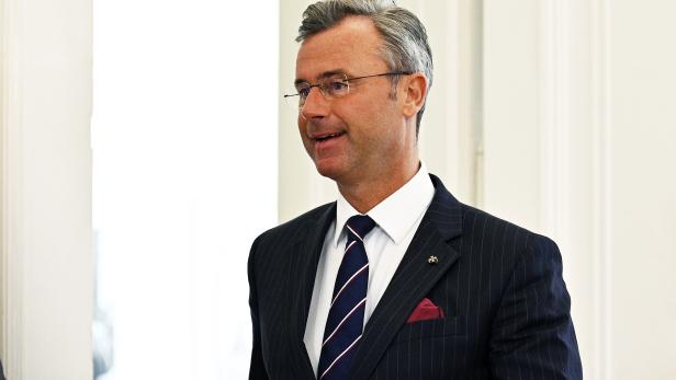 Ein Mann mit Brille trägt einen dunkel gestreiften Anzug, ein weißes Hemd und eine gestreifte Krawatte.