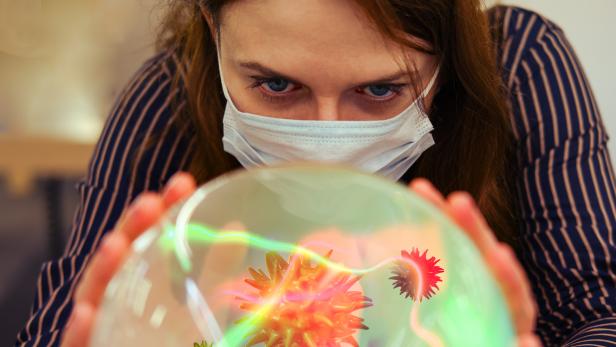 Eine Frau sieht in eine Glaskugel mit einem Virus.