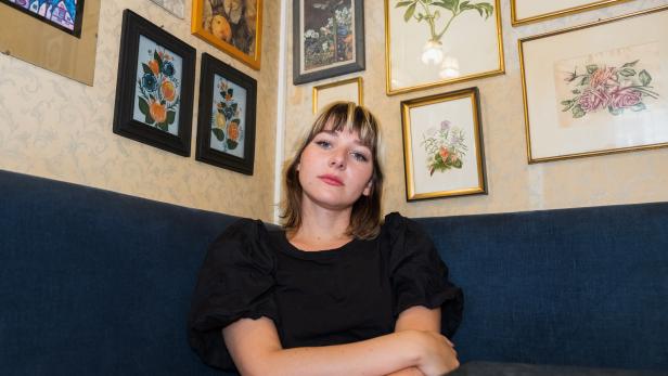 Eine junge Frau sitzt vor einer Wand mit gerahmten Bildern.
