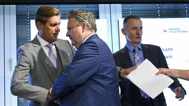 Zwei Männer in Anzügen schütteln sich die Hände vor einem Wiener Stadtwerke-Logo.