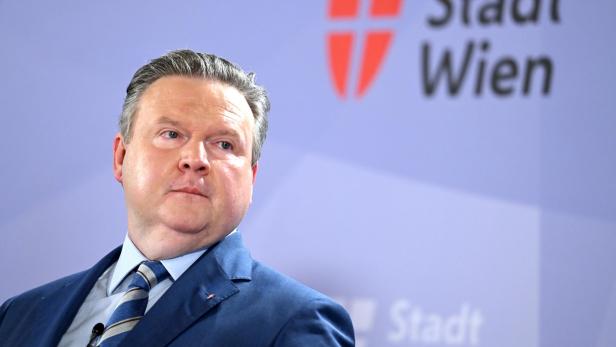 Ein Mann im Anzug vor dem Logo der Stadt Wien.