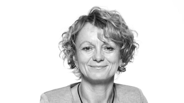 Porträt einer lächelnden Frau mit lockigem Haar und einer Halskette.