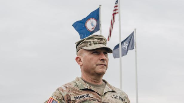 Ein Soldat der US-Armee in Uniform vor Flaggen, darunter die der USA und der NATO.