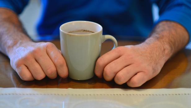 Ein Mann hält eine Tasse Kaffee auf einem Holztisch.