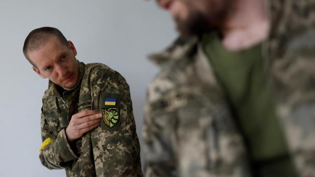 Ein ukrainischer Soldat mit Tarnuniform zeigt ein Abzeichen mit der ukrainischen Flagge.